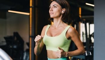 2127462771-fit-caucasian-beautiful-woman-fitting-sport-wear-gym-running-jogging-treadmill-with-wireless-headphones-ears-scaled-1