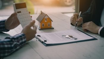 Real estate professionals offer their clients contracts to discuss home purchases, insurance or real estate loans. Home sales agents sit at the office with new home buyers in the office.