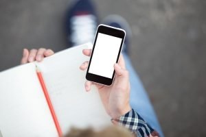 hand-holding-smartphone-against-copybook-with-pencil