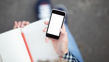 hand-holding-smartphone-against-copybook-with-pencil