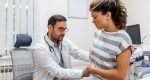 Patient telling physician about her pain and health problems during visit to hospital. Young woman complaining about back or kidney ache while sitting on examination bed at the doctor's office