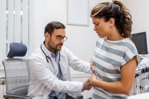 Patient telling physician about her pain and health problems during visit to hospital. Young woman complaining about back or kidney ache while sitting on examination bed at the doctor's office